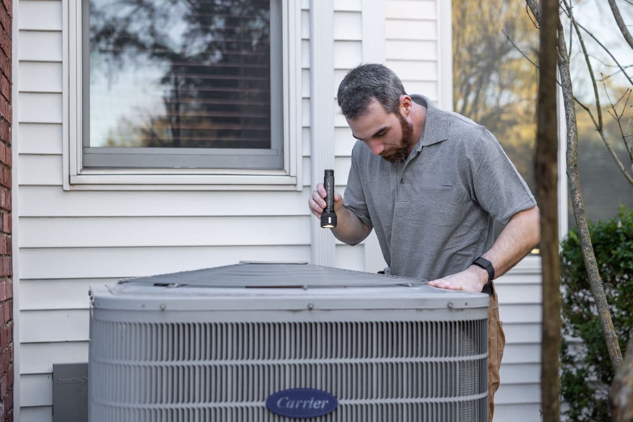 Technician inspecting a Carrier AC unit outside a home